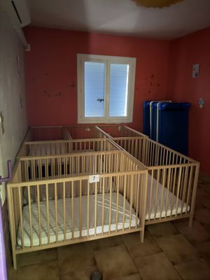 deux lits bébé dans une chambre avec une fenêtre et une poubelle