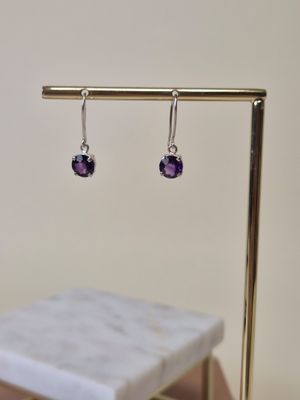 Boucles d'oreilles « Amethorate » sur un présentoir plaqué or, posées sur une table en marbre