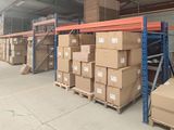 Les cartons sont empilés sur des palettes dans un grand entrepôt équipé de nombreuses étagères.