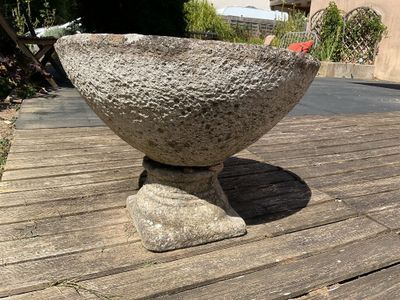 un bol en pierre posé sur une table en bois dans la cour