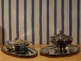 two silver dishes sitting on a table with blue and white striped wallpaper