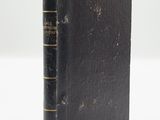 an old book with a black cover sitting on top of a white table