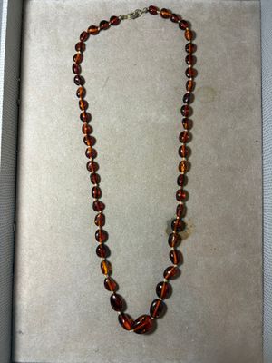 collier de perles en verre marron, présenté dans une boîte posée sur un fond blanc