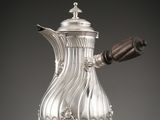 une cafetière en argent avec une poignée en bois, posée sur un socle