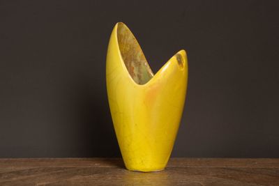un vase jaune posé sur une table, sur fond noir