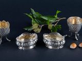 three silver dishes with spoons and spoons next to a plant
