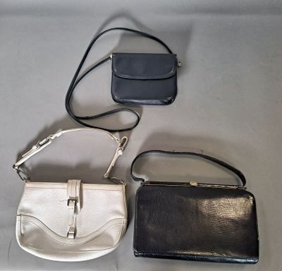 Trois sacs à main sont alignés sur une table : l'un est noir et l'autre est blanc.