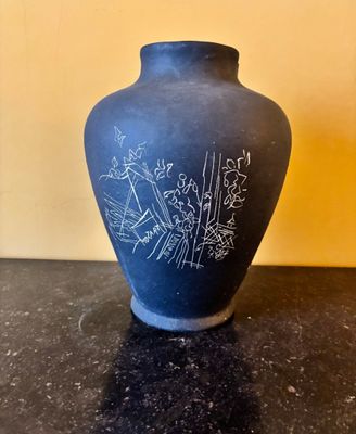 un vase noir orné d'un dessin, posé sur une table