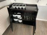 un petit meuble noir sur lequel sont posés de la vaisselle et des tasses