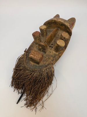 un vieux masque en bois accroché à un mur blanc