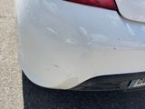 the rear end of a white car with a dent on it