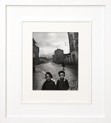 photographie en noir et blanc de deux personnes debout dans une rue pavée