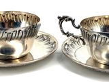 pair of silver plated cups and saucers on a white surface