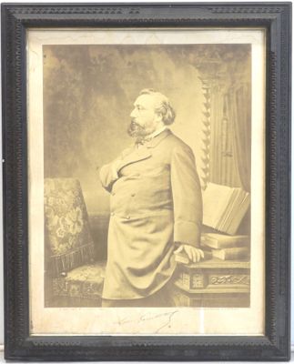une vieille photo d'un homme en costume debout devant une chaise