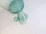 un vase en verre vert muni d'un couvercle, posé sur une table blanche
