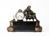 une statue représentant un homme assis sur une table, à côté d'une horloge