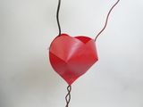 un cœur en papier rouge suspendu à un fil sur un mur blanc