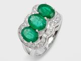 une bague à trois pierres, composée d'une émeraude et de diamants, sur fond blanc