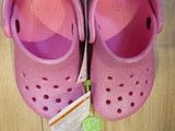 pair of pink crocs shoes on wooden floor next to luggage