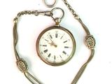 une montre de poche attachée à une chaîne, posée sur une surface blanche