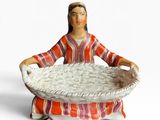 une figurine représentant une femme avec un panier sur les genoux