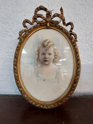 an old picture of a young girl in a blue dress in a gold frame