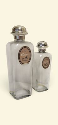 two clear glass bottles with silver lids on a white surface