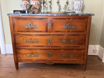une commode avec un plateau en marbre posée sur un parquet