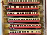 several red and yellow trains are in a wooden box on a white surface