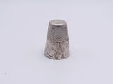a silver thimble sitting on a white surface