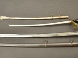 three swords are displayed on a gray surface with a gold handle