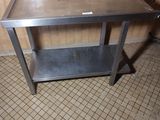 une table en métal avec une étagère posée dessus, dans une pièce