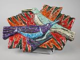 une assiette colorée ornée d'un oiseau, posée sur un socle