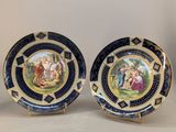 two blue and gold plates with paintings on them on a table