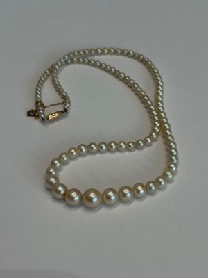 un collier de perles blanches muni d'un fermoir en or, posé sur un fond blanc