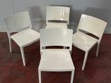 Quatre chaises en plastique blanc sont disposées en cercle sur un sol en briques.