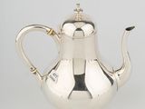 a silver tea pot with a handle and a handle on a white surface
