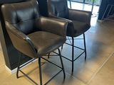 two black leather chairs sitting next to each other in front of a black wall