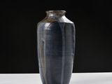un vase noir posé sur une table blanche, sur fond noir
