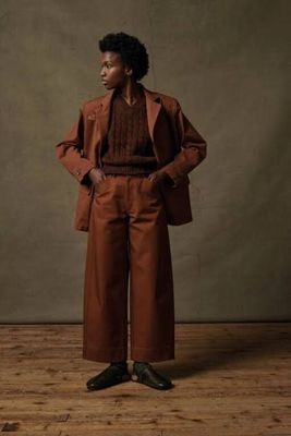 une photo d'une femme en tailleur marron, debout sur un parquet