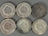 six types différents de pièces d'argent posées sur une surface grise