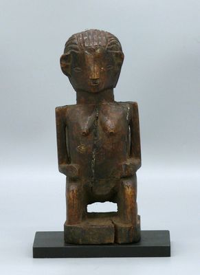 une vieille statue en bois représentant un homme assis sur un socle noir