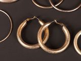 several pairs of gold hoop earrings on a black surface