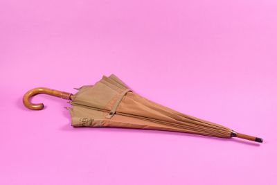 un parapluie marron avec un manche en bois sur fond rose