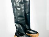 une paire de bottes en cuir noir à semelles en bois posées sur un socle blanc