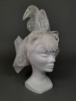 coiffe blanche ornée de dentelle et de plumes, posée sur une tête de mannequin