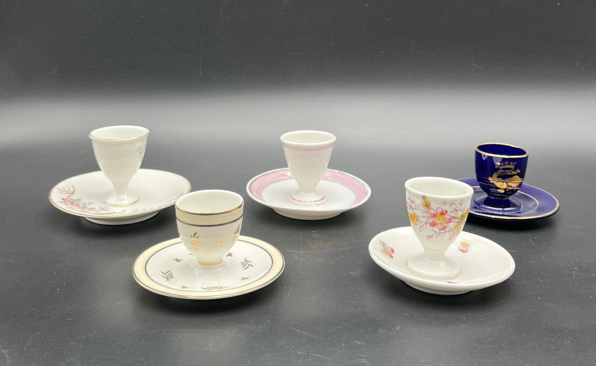 FRANCE (Tours Jaget et Pinon) Ensemble de cinq coquetiers à base en faïence et porcelaine à fond blanc et bleu à déco...