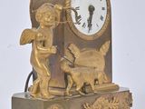 a gold clock with angels on it and a dog in front of it