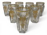 six glasses with gold designs are lined up on a white surface
