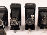 five old cameras are lined up in a row on a white surface